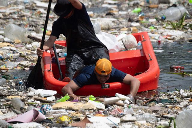 A worker on a plastic boat pushes rubbish washed up on a river at the height of heavy rains enhanced by the Southwest monsoon days before, near a shopping complex in Paranaque City, suburban Manila on August 11, 2026. Floods, landslides and accidents driven by a nine-day downpour equivalent to more than a month's worth of rain in some areas have killed at least 16 people in the northern Philippines, rescuers said on August 10. (Photo by Ted ALJIBE / AFP)