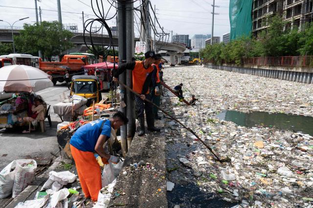 Workers scoop rubbish washed up on a river at the height of heavy rains enhanced by the Southwest monsoon days before, near a shopping complex in Paranaque City, suburban Manila on August 11, 2026. Floods, landslides and accidents driven by a nine-day downpour equivalent to more than a month's worth of rain in some areas have killed at least 16 people in the northern Philippines, rescuers said on August 10. (Photo by Ted ALJIBE / AFP)