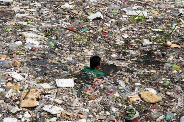 TOPSHOT - A worker swims amongst the rubbish washed up on a river at the height of heavy rains enhanced by the Southwest monsoon days before, near a shopping complex in Paranaque City, suburban Manila on August 11, 2026. Floods, landslides and accidents driven by a nine-day downpour equivalent to more than a month's worth of rain in some areas have killed at least 16 people in the northern Philippines, rescuers said on August 10. (Photo by Ted ALJIBE / AFP)