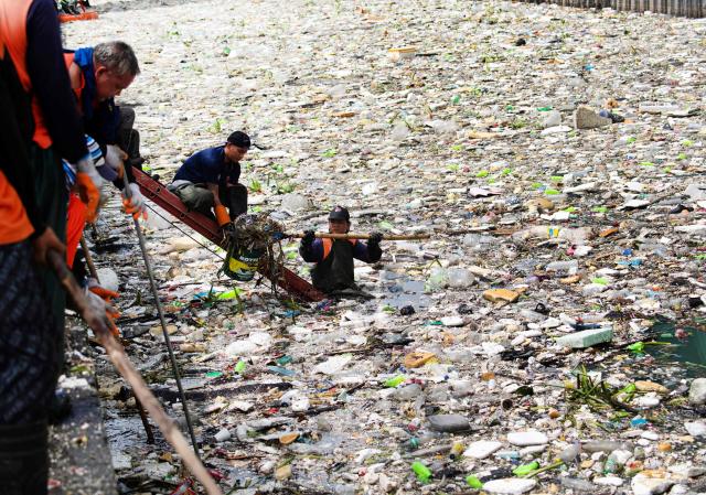 A worker collects rubbish washed up on a river at the height of heavy rains enhanced by the Southwest monsoon days before, near a shopping complex in Paranaque City, suburban Manila on August 11, 2026. Floods, landslides and accidents driven by a nine-day downpour equivalent to more than a month's worth of rain in some areas have killed at least 16 people in the northern Philippines, rescuers said on August 10. (Photo by Ted ALJIBE / AFP)