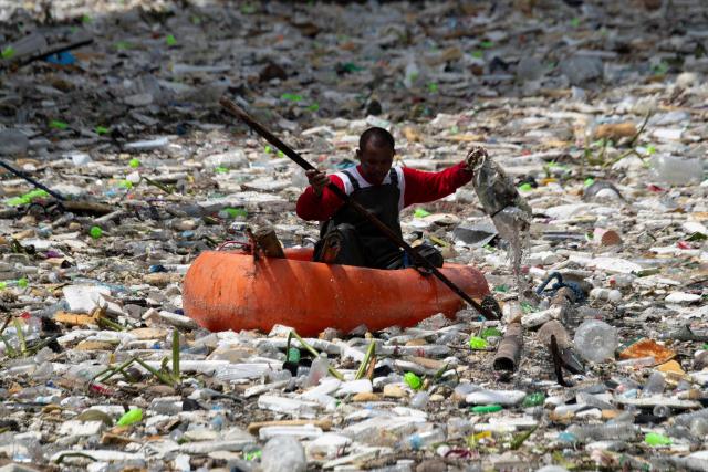 A worker on a plastic boat collects rubbish washed up on a river at the height of heavy rains enhanced by the Southwest monsoon days before, near a shopping complex in Paranaque City, suburban Manila on August 11, 2026. Floods, landslides and accidents driven by a nine-day downpour equivalent to more than a month's worth of rain in some areas have killed at least 16 people in the northern Philippines, rescuers said on August 10. (Photo by Ted ALJIBE / AFP)