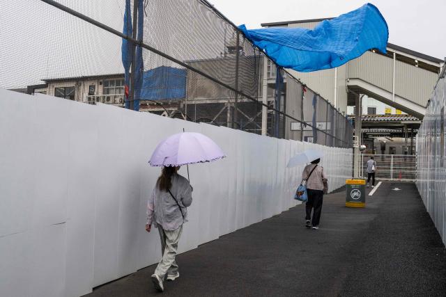 Two women pass under a contruction tarp blowing in gusting winds as Tropical Storm Chan-hom approaches Tokyo on August 11, 2026. (Photo by Andrew CABALLERO-REYNOLDS / AFP)
