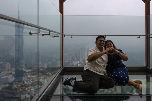 Visitors take pictures from the KL Tower as Warisan Merdeka Tower (KL118) (L) and commercial buildings are covered in haze in Kuala Lumpur on August 11, 2026, as authorities in Malaysia warned of high levels of air pollution from regional wildfires. The Malaysian Meteorological Department urged people on August 11 affected by air pollution to stay indoors, with director-general Mohd Hisham Mohd Anip blaming a "cross-border haze phenomenon from Kalimantan," the Indonesian portion of the island of Borneo. (Photo by Mohd Rasfan / AFP)