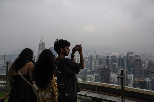 Visitors take pictures from the KL Tower as the Petronas Twin Towers and commercial buildings are covered in haze in Kuala Lumpur on August 11, 2026, as authorities in Malaysia warned of high levels of air pollution from regional wildfires. The Malaysian Meteorological Department urged people on August 11 affected by air pollution to stay indoors, with director-general Mohd Hisham Mohd Anip blaming a "cross-border haze phenomenon from Kalimantan," the Indonesian portion of the island of Borneo. (Photo by Mohd Rasfan / AFP)