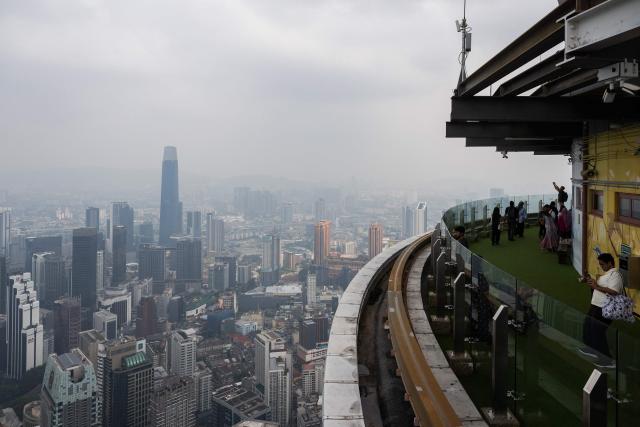 Visitors take pictures from the Kl Tower as the city is covered in haze in Kuala Lumpur on August 11, 2026, as authorities in Malaysia warned of high levels of air pollution from regional wildfires. The Malaysian Meteorological Department urged people on August 11 affected by air pollution to stay indoors, with director-general Mohd Hisham Mohd Anip blaming a "cross-border haze phenomenon from Kalimantan," the Indonesian portion of the island of Borneo. (Photo by Mohd Rasfan / AFP)