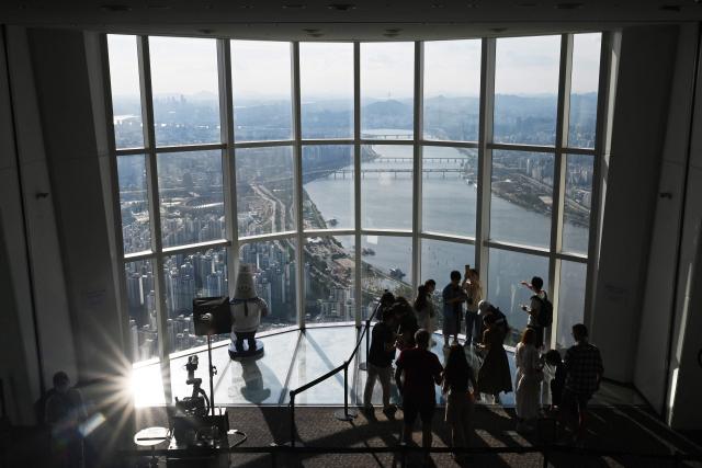 People look at views across the city from an observation deck at the Lotte World Tower in Seoul on August 11, 2026. (Photo by GREG BAKER / AFP)