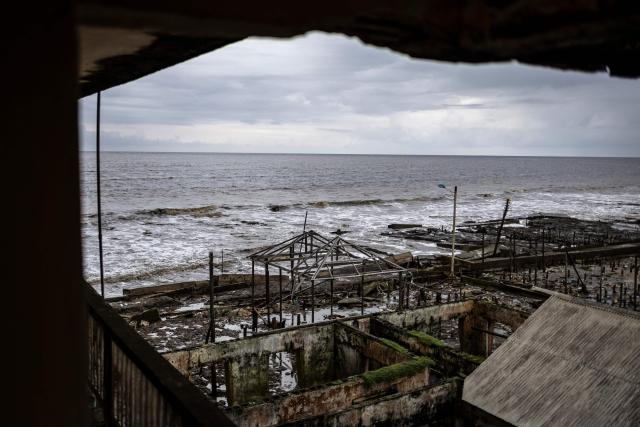 TOPSHOT - A general view of buildings destroyed by coastal erosion, seen from the King's Palace in Ayetoro, Ondo State, on August 6, 2026. The coastal community of Ayetoro, in Nigeria's southwestern Ondo State, has become one of the country's most visible examples of the vulnerability of communities living along the Atlantic Ocean to coastal erosion and rising waters. Since the early 2000s, coastal erosion in Ayetoro has progressively intensified, with the Atlantic Ocean gradually encroaching on the settlement, swallowing homes, schools, and other infrastructure, and forcing some residents to relocate several times. The ocean that the community has lived alongside for generations has become a constant threat, leaving families to rebuild further inland only to see the water reach them again. For many in Ayetoro, the question is no longer whether the sea will reach their home, but when. (Photo by OLYMPIA DE MAISMONT / AFP)