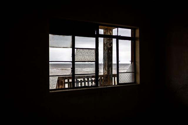 A general view of the Atlantic Ocean through the windows of the King's Palace, which has been damaged by coastal erosion, in Ayetoro, Ondo State, on August 6, 2026. The coastal community of Ayetoro, in Nigeria's southwestern Ondo State, has become one of the country's most visible examples of the vulnerability of communities living along the Atlantic Ocean to coastal erosion and rising waters. Since the early 2000s, coastal erosion in Ayetoro has progressively intensified, with the Atlantic Ocean gradually encroaching on the settlement, swallowing homes, schools, and other infrastructure, and forcing some residents to relocate several times. The ocean that the community has lived alongside for generations has become a constant threat, leaving families to rebuild further inland only to see the water reach them again. For many in Ayetoro, the question is no longer whether the sea will reach their home, but when. (Photo by OLYMPIA DE MAISMONT / AFP)
