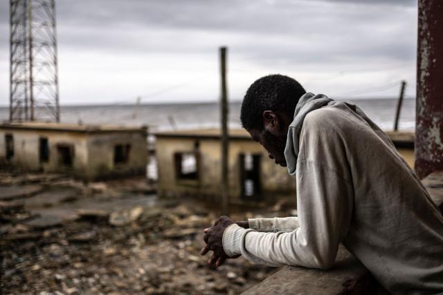 A resident looks at buildings destroyed by coastal erosion from the King's Palace in Ayetoro, Ondo State, on August 6, 2026. The coastal community of Ayetoro, in Nigeria's southwestern Ondo State, has become one of the country's most visible examples of the vulnerability of communities living along the Atlantic Ocean to coastal erosion and rising waters. Since the early 2000s, coastal erosion in Ayetoro has progressively intensified, with the Atlantic Ocean gradually encroaching on the settlement, swallowing homes, schools, and other infrastructure, and forcing some residents to relocate several times. The ocean that the community has lived alongside for generations has become a constant threat, leaving families to rebuild further inland only to see the water reach them again. For many in Ayetoro, the question is no longer whether the sea will reach their home, but when. (Photo by OLYMPIA DE MAISMONT / AFP)