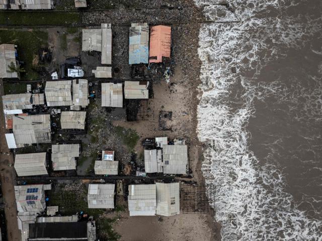 An aerial view shows houses along the shoreline affected by coastal erosion in Ayetoro, Ondo State, on August 7, 2026. The coastal community of Ayetoro, in Nigeria's southwestern Ondo State, has become one of the country's most visible examples of the vulnerability of communities living along the Atlantic Ocean to coastal erosion and rising waters. Since the early 2000s, coastal erosion in Ayetoro has progressively intensified, with the Atlantic Ocean gradually encroaching on the settlement, swallowing homes, schools, and other infrastructure, and forcing some residents to relocate several times. The ocean that the community has lived alongside for generations has become a constant threat, leaving families to rebuild further inland only to see the water reach them again. For many in Ayetoro, the question is no longer whether the sea will reach their home, but when. (Photo by OLYMPIA DE MAISMONT / AFP)
