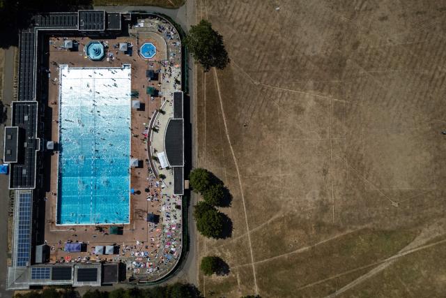 An aerial view shows swimmers using Parliament Hill Fields Lido in London on August 11, 2026, following weeks of hot, dry weather, with nearly three quarters of England being classified as in drought. Some 71.3 percent of England is in drought, the UK government said Monday, after the nation experienced its driest July on record, with a fifth heatwave and scant rain forecast for the week ahead. (Photo by HENRY NICHOLLS / AFP)