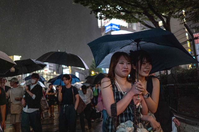 Pedestrians use umbrellas to shelter from the rain while walking on a street in Shinjuku district in Tokyo on August 11, 2026. (Photo by Philip FONG / AFP)