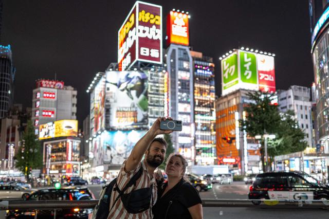 People take pictures in Shinjuku district in Tokyo on August 11, 2026. (Photo by Philip FONG / AFP)