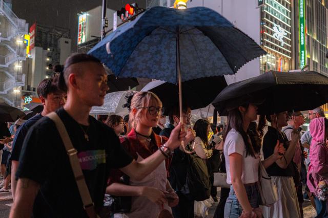 Pedestrians use umbrellas to shelter from the rain while walking on a street in Shinjuku district in Tokyo on August 11, 2026. (Photo by Philip FONG / AFP)