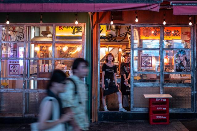 Restaurant staff look out from a doorway of their establishment in Shinjuku district in Tokyo on August 11, 2026. (Photo by Philip FONG / AFP)
