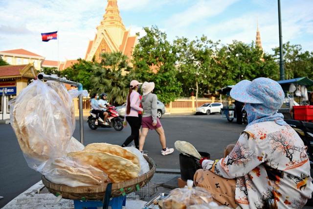 A vendor grills a rice cake known as nom kreap for sale along a street in front of the Supreme Court in Phnom Penh on August 11, 2026.  (Photo by TANG CHHIN Sothy / AFP)