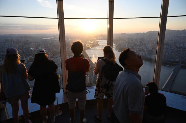 People look at views across the city from an observation deck at the Lotte World Tower at sunset in Seoul on August 11, 2026. (Photo by GREG BAKER / AFP)