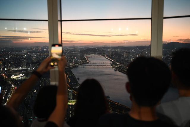 People look at views across the city from an observation deck at the Lotte World Tower at dusk in Seoul on August 11, 2026. (Photo by GREG BAKER / AFP)