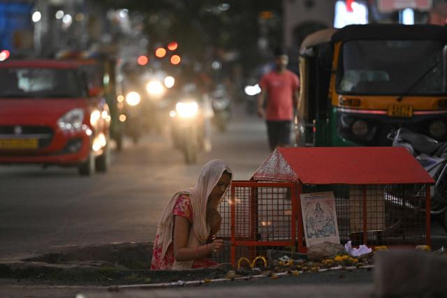A woman offers prayers at a roadside Hindu shrine as commuters ride past in Bengaluru on August 11, 2026. (Photo by Idrees MOHAMMED / AFP)