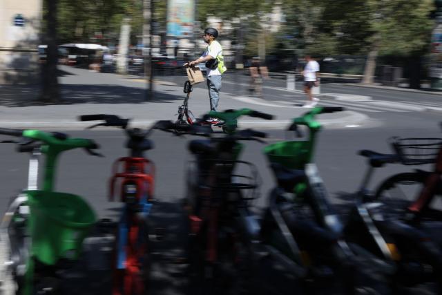 A man with a helmet and a reflective gear rides an electric scooter past traffic on a street of Paris on August 11, 2026. Electric scooter riders in Paris must now wear helmets and reflective gear under new rules introduced after a significant rise in injuries involving the two-wheelers, police said on August 8, 2026. (Photo by Kenzo TRIBOUILLARD / AFP)