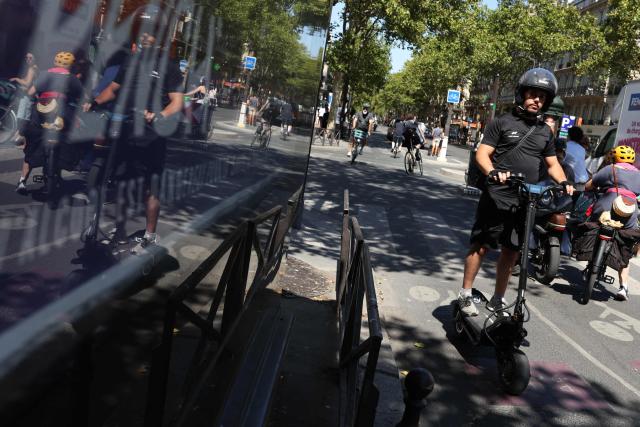 A man with a helmet rides an electric scooter past traffic on a street of Paris on August 11, 2026. Electric scooter riders in Paris must now wear helmets and reflective gear under new rules introduced after a significant rise in injuries involving the two-wheelers, police said on August 8, 2026. (Photo by Kenzo TRIBOUILLARD / AFP)
