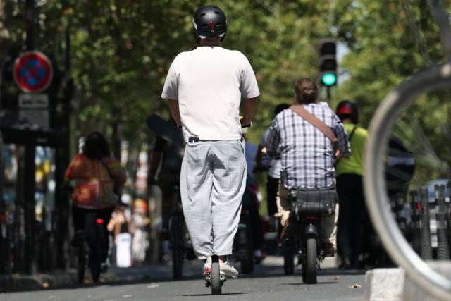 A man rides an electric scooter past traffic on a street of Paris on August 11, 2026. Electric scooter riders in Paris must now wear helmets and reflective gear under new rules introduced after a significant rise in injuries involving the two-wheelers, police said on August 8, 2026. (Photo by Kenzo TRIBOUILLARD / AFP)