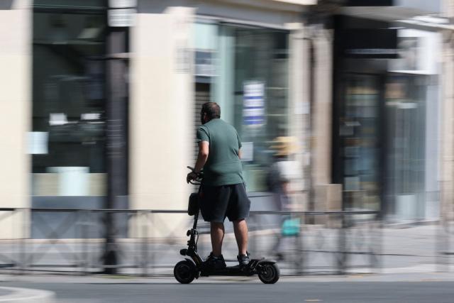 A man rides an electric scooter past traffic on a street of Paris on August 11, 2026. Electric scooter riders in Paris must now wear helmets and reflective gear under new rules introduced after a significant rise in injuries involving the two-wheelers, police said on August 8, 2026. (Photo by Kenzo TRIBOUILLARD / AFP)