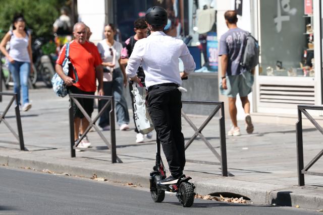 A man with a helmet rides an electric scooter past traffic on a street of Paris on August 11, 2026. Electric scooter riders in Paris must now wear helmets and reflective gear under new rules introduced after a significant rise in injuries involving the two-wheelers, police said on August 8, 2026. (Photo by Kenzo TRIBOUILLARD / AFP)