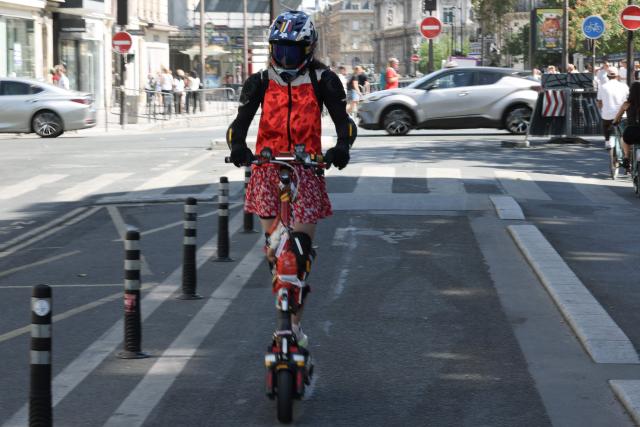 A woman with a helmet rides an electric scooter past traffic on a street of Paris on August 11, 2026. Electric scooter riders in Paris must now wear helmets and reflective gear under new rules introduced after a significant rise in injuries involving the two-wheelers, police said on August 8, 2026. (Photo by Kenzo TRIBOUILLARD / AFP)