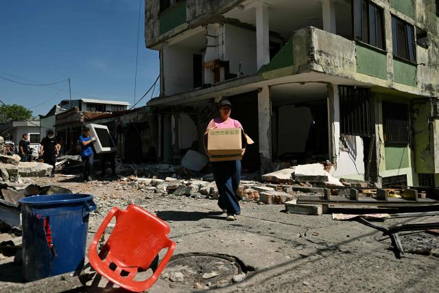 A woman carrying a box walks past a collapsed building following an earthquake in Pereira, Colombia on August 11, 2026. Colombian volunteers and rescuers cleared rubble with their bare hands to search for survivors early on August 11 after the country's strongest earthquake in a decade killed at least 169 people and smashed dozens of buildings. (Photo by Luis ACOSTA / AFP)