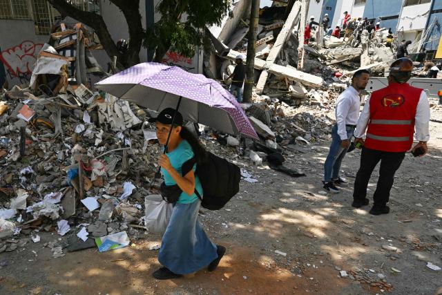 A woman using an umbrella walks past the rubble of a collapsed building following an earthquake in Pereira, Colombia on August 11, 2026. Colombian volunteers and rescuers cleared rubble with their bare hands to search for survivors early on August 11 after the country's strongest earthquake in a decade killed at least 169 people and smashed dozens of buildings. (Photo by Luis ACOSTA / AFP)