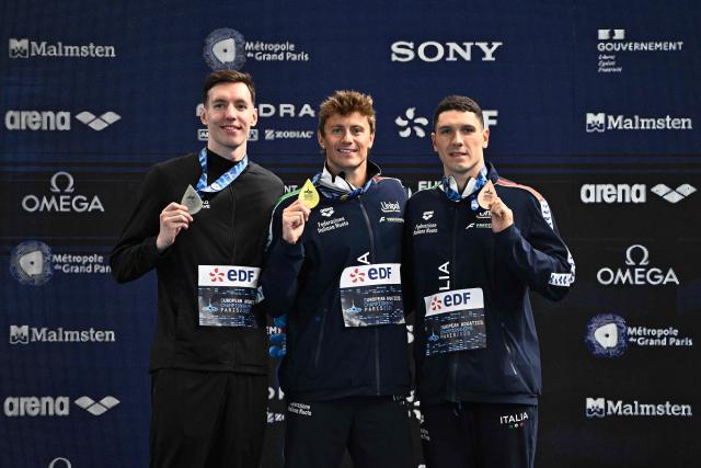 Gold medallist Italy's Nicolo Martinenghi (C), silver medallist Neutral Athlete B's Ivan Kozhakin (L) and bronze medallist Italy's Simone Cerasuolo (R) pose on the podium of the men's 100m breaststroke swimming event during the LEN European Aquatics Championships at the Olympic Aquatic Centre in Saint-Denis, northern suburbs of Paris, on August 11, 2026. (Photo by JULIEN DE ROSA / AFP)