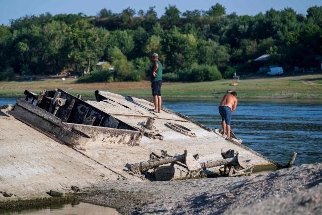 This photograph shows people exploring the wreckage of a World War II German warship, one of dozens sunk by retreating Nazi forces in September 1944, emerging from the low waters of the Danube River near Prahovo, Serbia, on August 11, 2026, as drought and prolonged hot and dry weather continues to lower water levels across the region. Heat and drought are driving rivers across Europe to record lows. Low levels along the Danube river have already seen Hungary and Romania forced to consider shuttering their nuclear plants, which rely on the water for cooling, in late July, though both managed to avoid doing so for now. (Photo by Andrej ISAKOVIC / AFP)