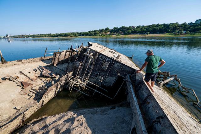 This photograph shows a man exploring the wreckage of a World War II German warship, one of dozens sunk by retreating Nazi forces in September 1944, emerging from the low waters of the Danube River near Prahovo, Serbia, on August 11, 2026, as drought and prolonged hot and dry weather continues to lower water levels across the region. Heat and drought are driving rivers across Europe to record lows. Low levels along the Danube river have already seen Hungary and Romania forced to consider shuttering their nuclear plants, which rely on the water for cooling, in late July, though both managed to avoid doing so for now. (Photo by Andrej ISAKOVIC / AFP)