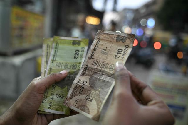 A vendor counts ten and twenty-rupee banknotes at a roadside stall in Bengaluru on August 11, 2026 following approval for field trials of polymer versions of the notes. (Photo by Idrees MOHAMMED / AFP)