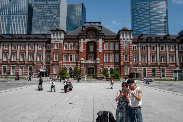 People take pictures in front of Tokyo station on August 12, 2026. (Photo by Philip FONG / AFP)
