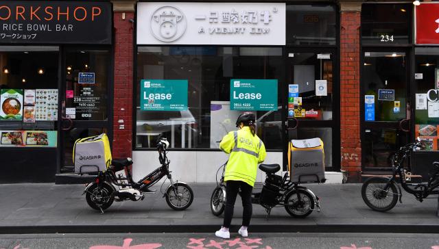 (FILES) A food delivery rider picks up an order in Melbourne's Chinatown on October 19, 2021. Hundreds of thousands of gig workers in Australia have been granted a huge pay rise from August 17, 2026 under a decision by the country's workplace relations tribunal lauded as "world-leading". (Photo by William WEST / AFP)
