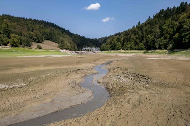 This aerial photograph shows the parched bed of Brenets Lake (Lac des Brenets), part of the Doubs River, a natural border between eastern France and western Switzerland, as central Europe is hit by a new heatwave, in Les Brenets on August 11, 2026. The river has dried up due to a combination of factors, including geological fissures that drain water underground, below-average rainfall and repeated heatwaves. (Photo by Fabrice COFFRINI / AFP)