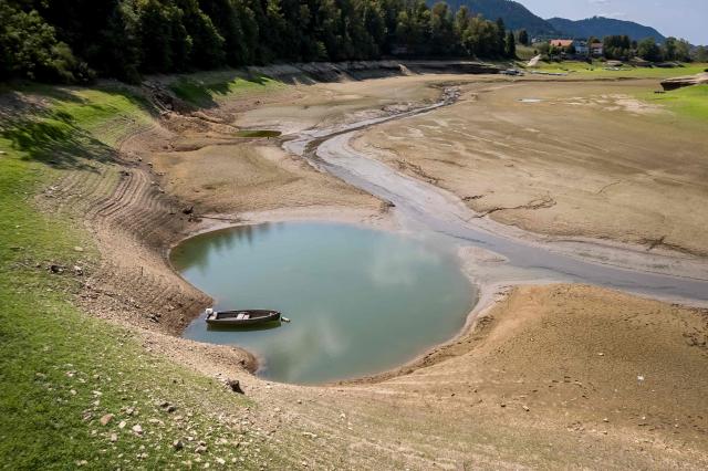 This aerial photograph shows the parched bed of Brenets Lake (Lac des Brenets), part of the Doubs River, a natural border between eastern France and western Switzerland, as central Europe is hit by a new heatwave, in Les Brenets on August 11, 2026. The river has dried up due to a combination of factors, including geological fissures that drain water underground, below-average rainfall and repeated heatwaves. (Photo by Fabrice COFFRINI / AFP)