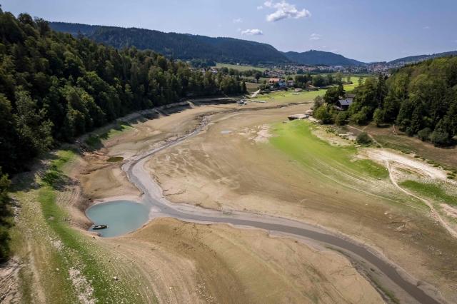 This aerial photograph shows the parched bed of Brenets Lake (Lac des Brenets), part of the Doubs River, a natural border between eastern France and western Switzerland, as central Europe is hit by a new heatwave, in Les Brenets on August 11, 2026. The river has dried up due to a combination of factors, including geological fissures that drain water underground, below-average rainfall and repeated heatwaves. (Photo by Fabrice COFFRINI / AFP)