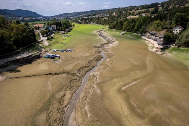 This aerial photograph shows the parched bed of Brenets Lake (Lac des Brenets), part of the Doubs River, a natural border between eastern France and western Switzerland, as central Europe is hit by a new heatwave, in Les Brenets on August 11, 2026. The river has dried up due to a combination of factors, including geological fissures that drain water underground, below-average rainfall and repeated heatwaves. (Photo by Fabrice COFFRINI / AFP)
