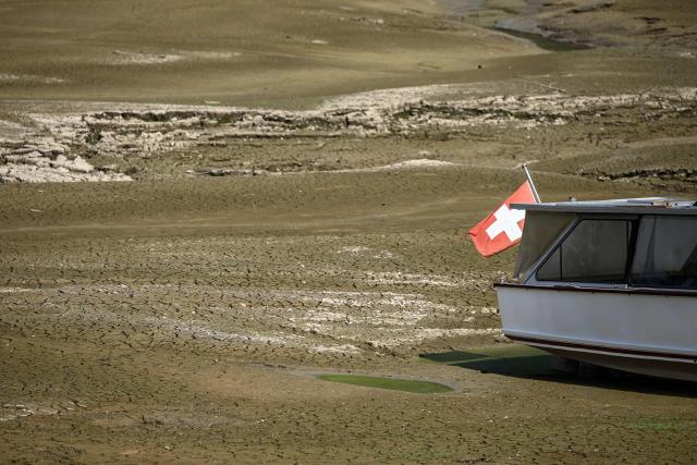 This photograph shows a Swiss flag flying at the stern of a boat stranded on the lakebed of Brenets Lake (Lac des Brenets), part of the Doubs River, a natural border between eastern France and western Switzerland, as central Europe is hit by a new heatwave, in Les Brenets on August 11, 2026. The river has dried up due to a combination of factors, including geological fissures that drain water underground, below-average rainfall and repeated heatwaves. (Photo by Fabrice COFFRINI / AFP)