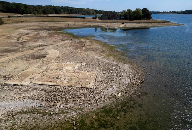An aerial view of Anglian Water's Rutland Water reservoir shows the remains of buildings in the former hamlet of Middle Hambleton, revealed in the bed of the reservoir by the receding water -- a reservoir created by the flooding of hamlets Lower and Middle Hambleton -- due to the persistent hot weather and drought, in Upper Hambleton, central England on August 12, 2026. England and Wales experienced their driest July on record this year, with high temperatures and low rainfall across swathes of the country having plunged almost three-quarters of England and all of Wales into drought. (Photo by HENRY NICHOLLS / AFP)