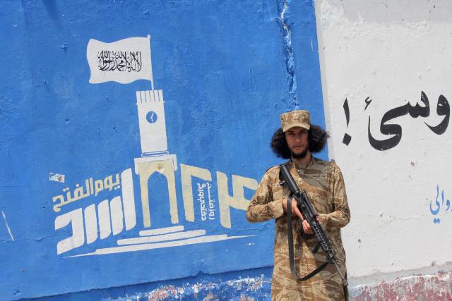 A security personnel stands guard next to a wall mural depicting the Taliban flag, along a street in Jalalabad on August 12, 2026 ahead of the fifth anniversary of their takeover of Afghanistan. (Photo by Aimal Zahir / AFP)
