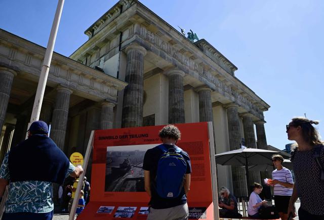 Visitors discover an outdoor exhibition on the Berlin wall in front of the Brandenburg Gate after a press conference about Berlin's program about the 65th anniversary of the construction of the Berlin Wall in Berlin, on August 12, 2026. (Photo by John MACDOUGALL / AFP) / ALTERNATIVE CROP
