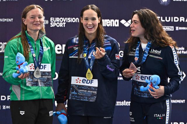 (LtoR) Ireland's Mona Mc Sharry (silver medal), Britain's Angharad Evans (gold medal) and Italy's Benedetta Pilato (bronze medal) pose during the podium ceremony of the women's 100m breaststroke swimming event during the LEN European Aquatics Championships at the Olympic Aquatic Centre in Saint-Denis, northern suburbs of Paris, on August 12, 2026. (Photo by JULIEN DE ROSA / AFP)