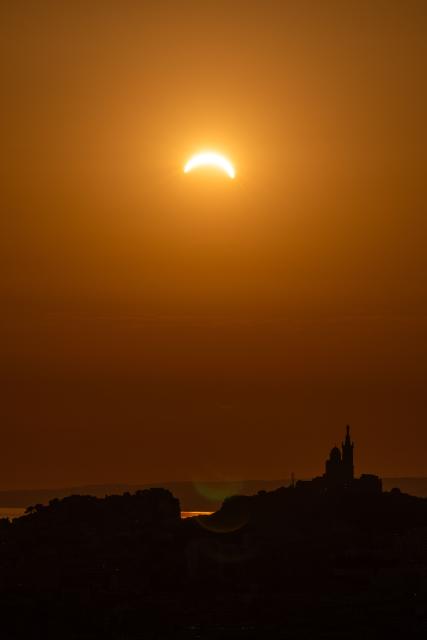The moon passes over the sun's horizon behind the Notre-Dame de la Garde Basilica, nicknamed the “Bonne Mиre,” during a partial solar eclipse in Marseille, in southeastern France, on August 12, 2026. In France, the solar eclipse was not total - after the total solar eclipse of 1999 France will not see another total eclipse for another 55 years in 2081. (Photo by Thibaud MORITZ / AFP)