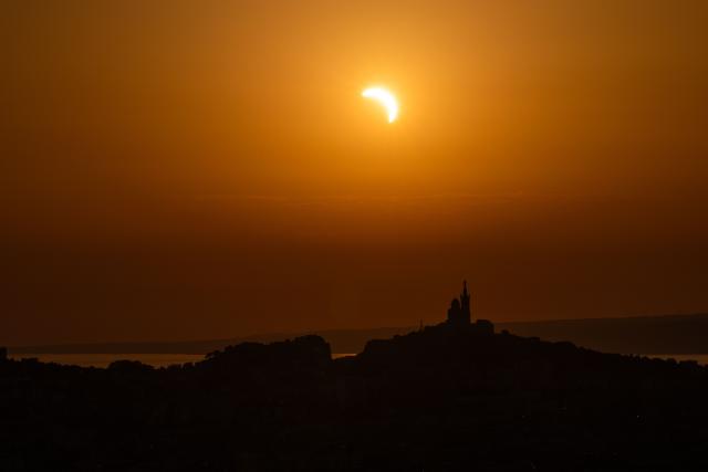 The moon passes over the sun's horizon behind the Notre-Dame de la Garde Basilica, nicknamed the “Bonne Mиre,” during a partial solar eclipse in Marseille, in southeastern France, on August 12, 2026. In France, the solar eclipse was not total - after the total solar eclipse of 1999 France will not see another total eclipse for another 55 years in 2081. (Photo by Thibaud MORITZ / AFP)