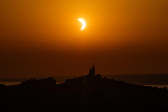 The moon passes over the sun's horizon behind the Notre-Dame de la Garde Basilica, nicknamed the “Bonne Mиre,” during a partial solar eclipse in Marseille, in southeastern France, on August 12, 2026. In France, the solar eclipse was not total - after the total solar eclipse of 1999 France will not see another total eclipse for another 55 years in 2081. (Photo by Thibaud MORITZ / AFP)