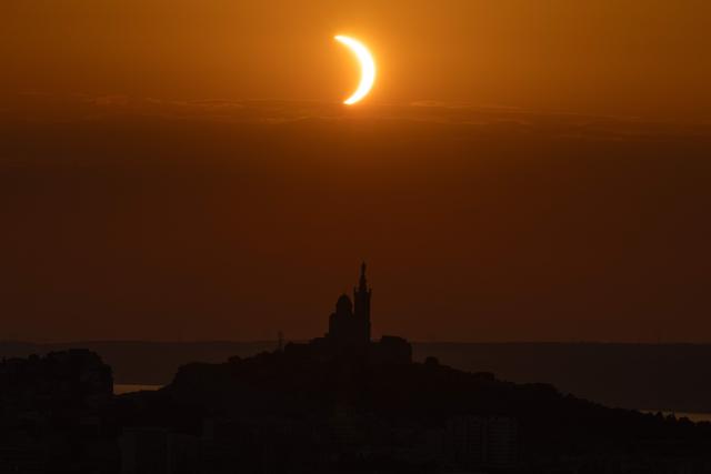The moon passes over the sun's horizon behind the Notre-Dame de la Garde Basilica, nicknamed the “Bonne Mиre,” during a partial solar eclipse in Marseille, in southeastern France, on August 12, 2026. In France, the solar eclipse was not total - after the total solar eclipse of 1999 France will not see another total eclipse for another 55 years in 2081. (Photo by Thibaud MORITZ / AFP)